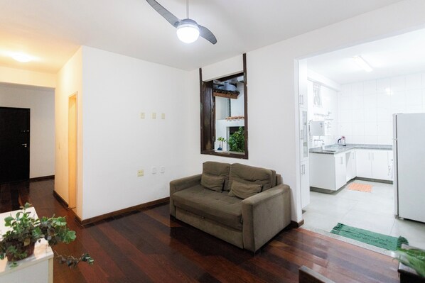 A living room with a sofa, a ceiling fan, and a view into the kitchen. - SUH Catete 06 Big House Metro (Rio de Janeiro)