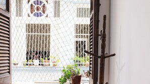 A wooden chair with a cushion, a coat rack, and a window with a view of a building. - SUH Catete 06 Big House Metro (Rio de Janeiro)