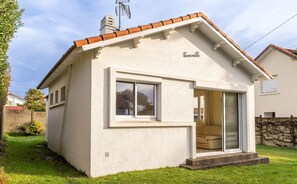A small, single-story house with a white exterior, a tiled roof, and a sliding glass door leading to an interior with a sofa. - Holiday Home 'Au Bercement par les vagues' with Private Garden – 80m from Beach (Pornic)