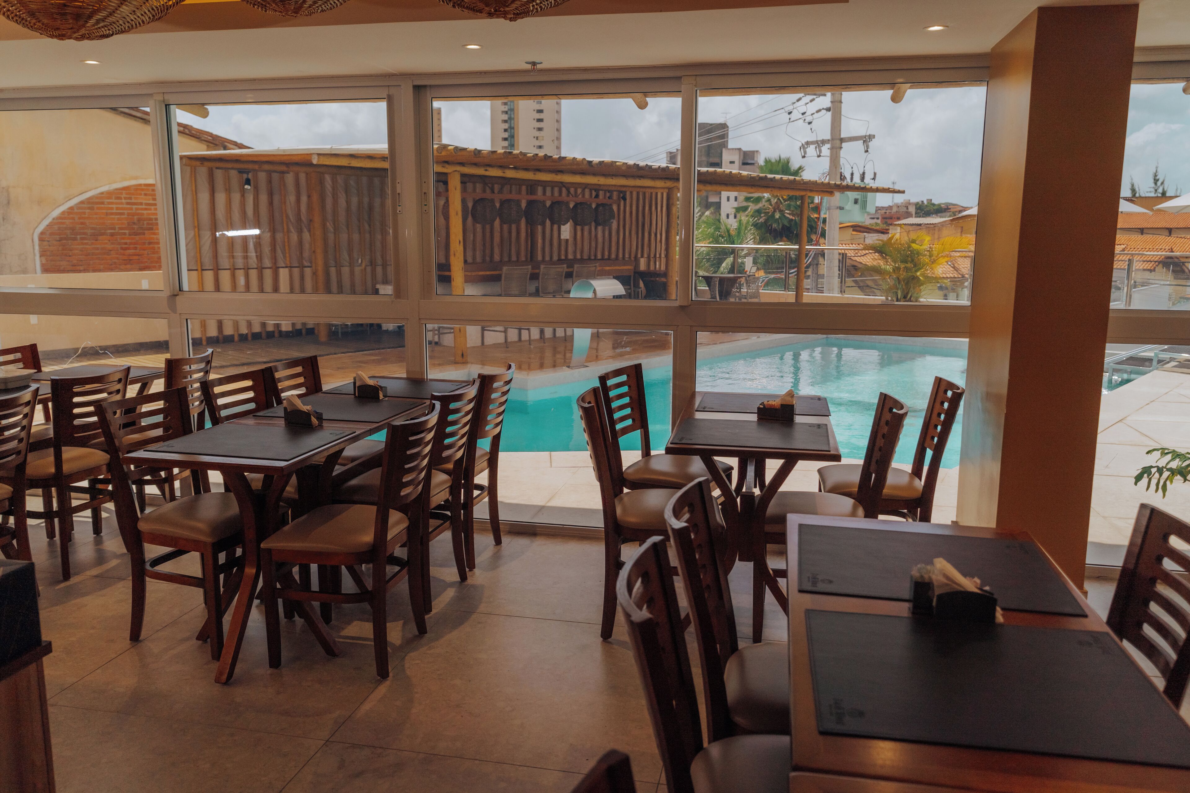 Restaurante com área externa e mesas de madeira, com vista para uma piscina.