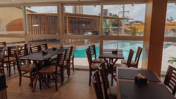 Restaurante com área externa e mesas de madeira, com vista para uma piscina.
