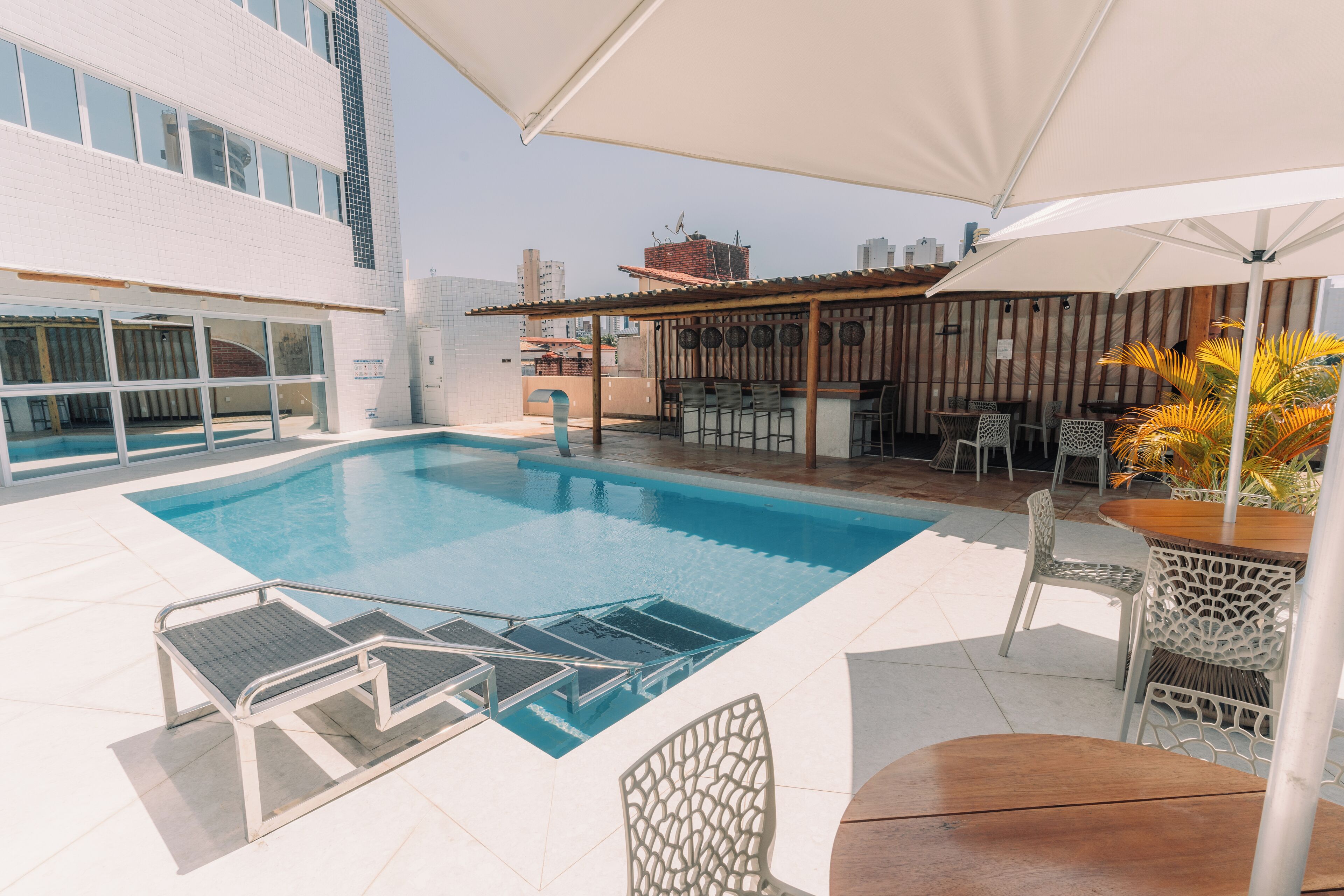 Zona de piscina en la azotea con trampolín, sillas de descanso y zona de bar.