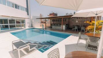 Zona de piscina en la azotea con trampolín, sillas de descanso y zona de bar.