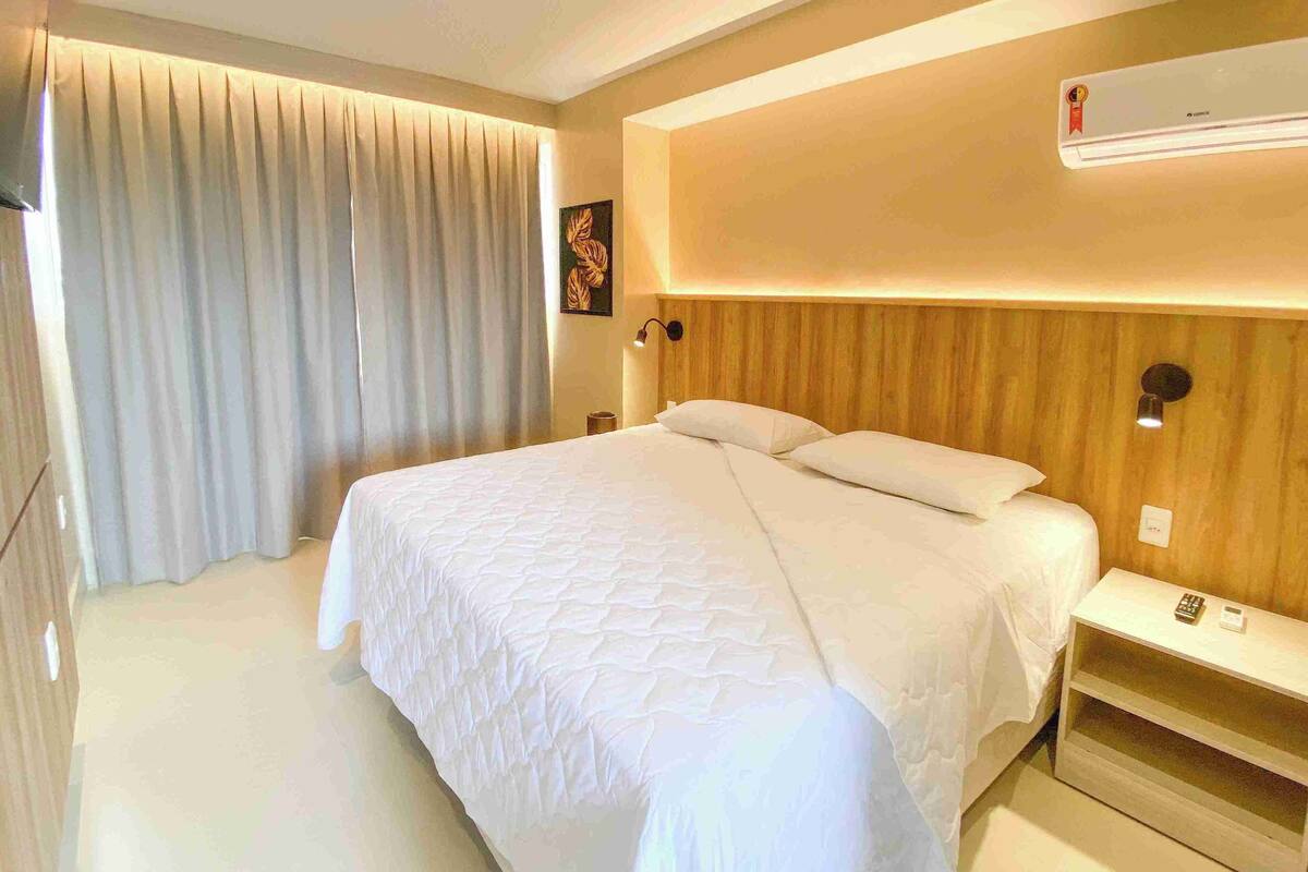 A modern hotel room with a large bed, a bedside table with a lamp, and an air conditioning unit on the wall.