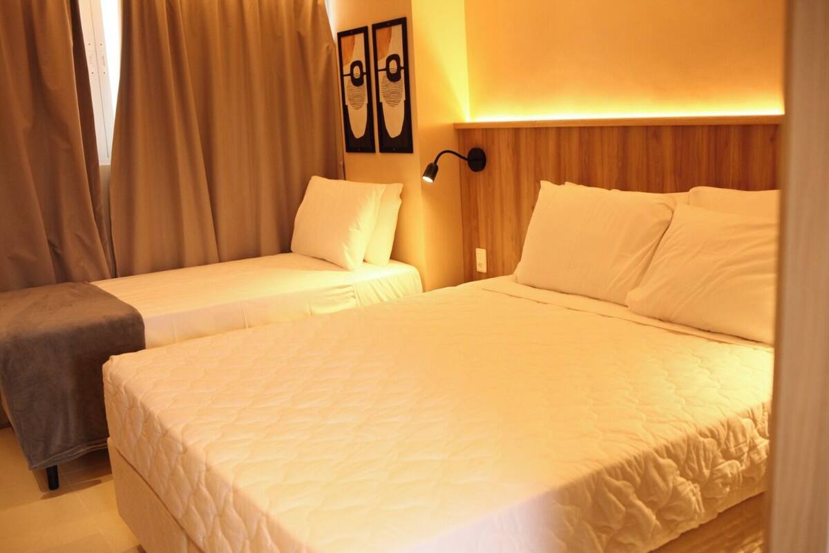 A hotel room with two beds, a nightstand, a wall-mounted lamp, and a painting.