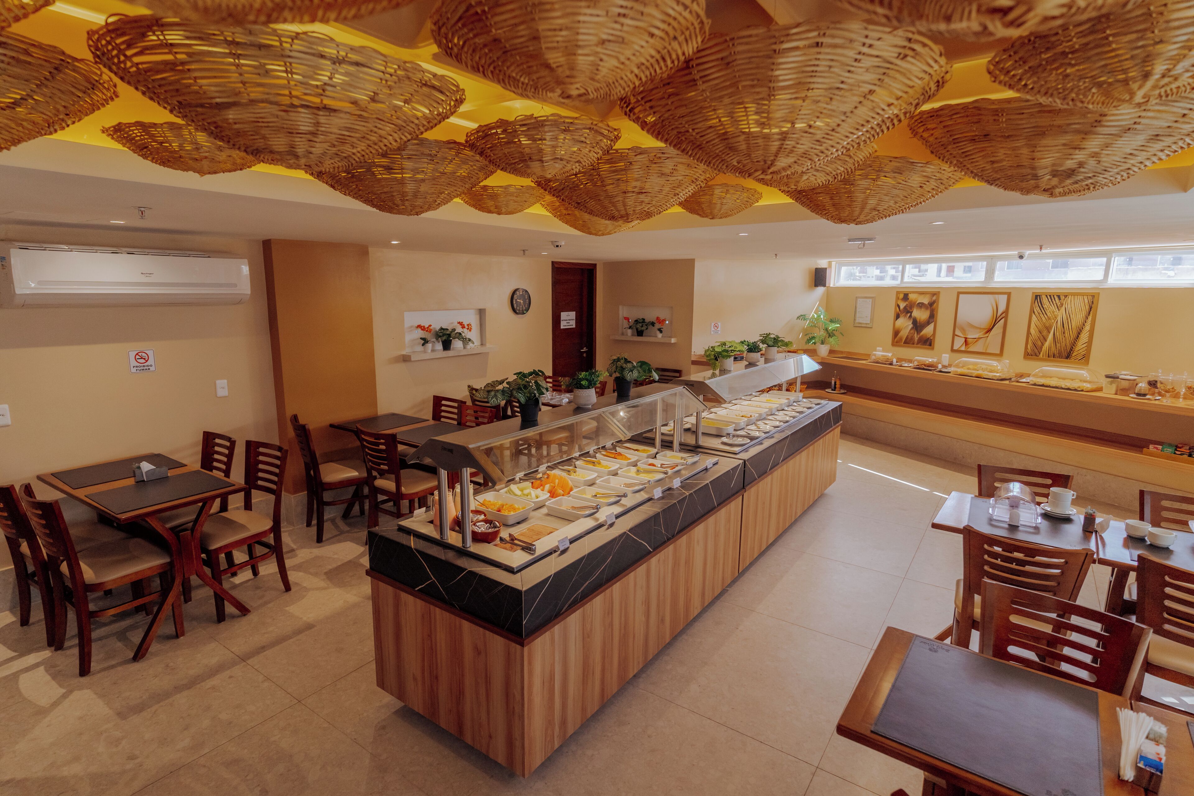 Uma área de buffet com ilha central, cadeiras de madeira e teto com cestos trançados.