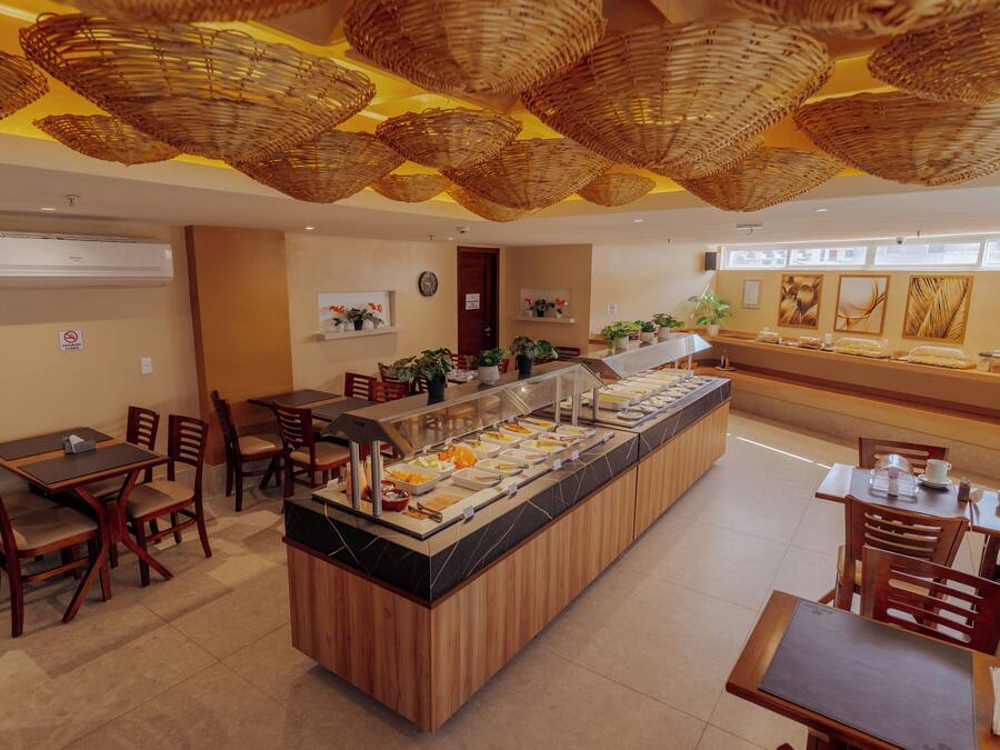 Uma área de buffet com ilha central, cadeiras de madeira e teto com cestos trançados.