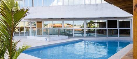 A modern building with a swimming pool, large windows, and a covered area with a wooden ceiling.