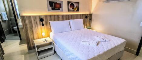 A neatly made bed with white linens, a bedside table with a lamp, and two wall-mounted artworks.