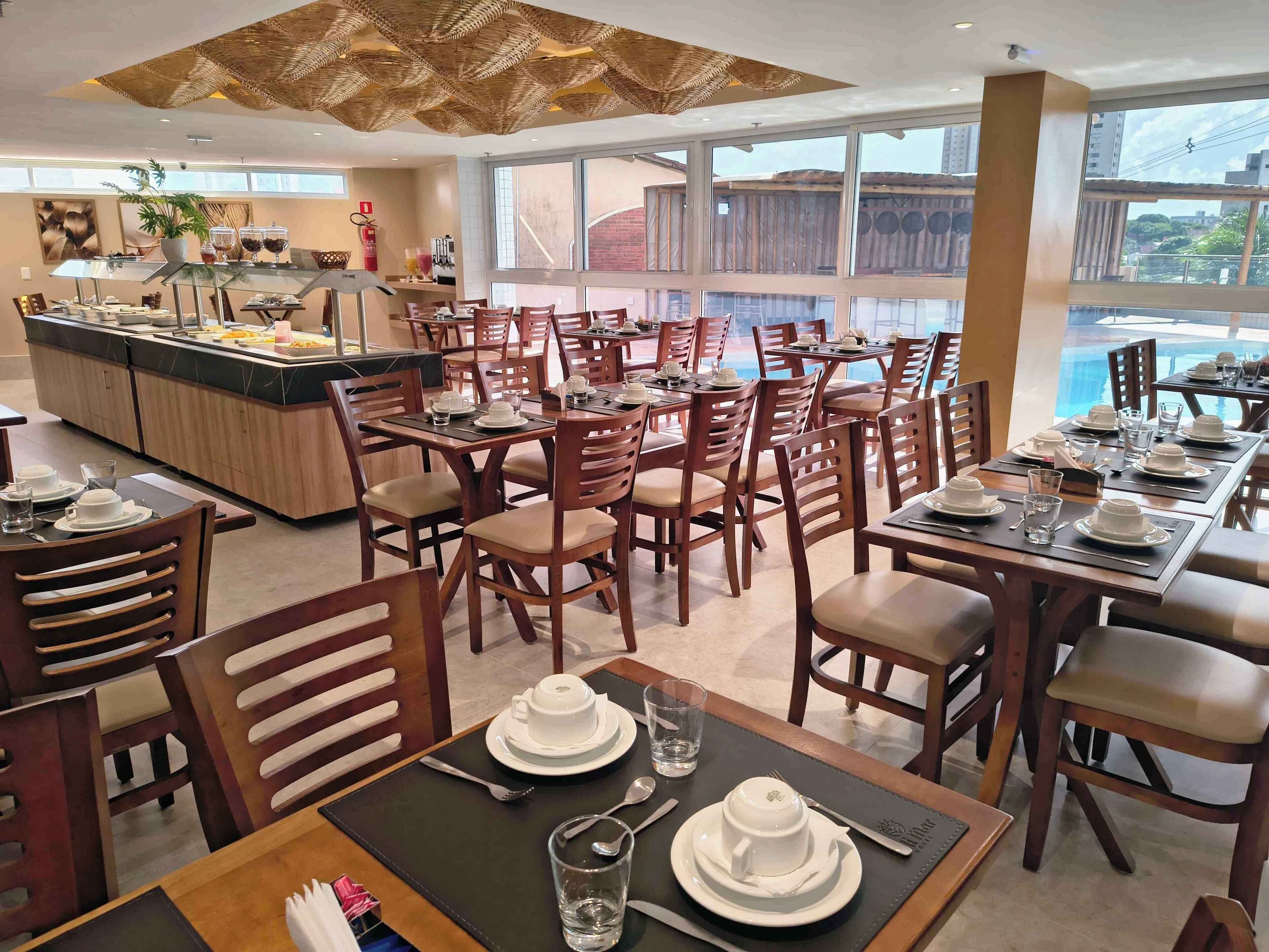 Un restaurante con varias mesas y sillas, una zona de bufé y amplias ventanas con vistas al exterior.