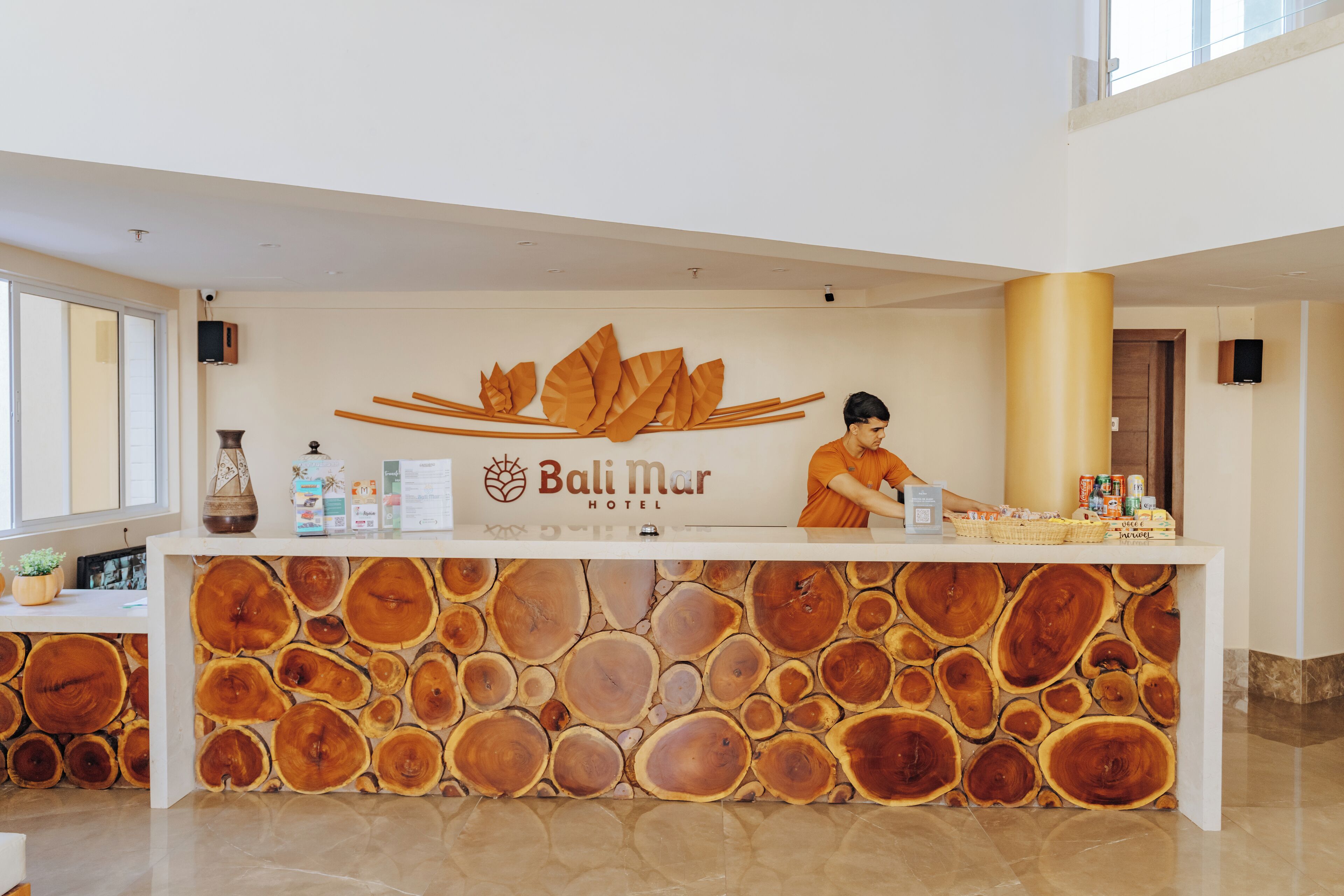 A hotel reception desk with a logo, a staff member, and a counter with various items.