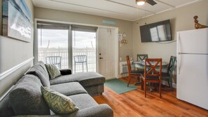 A living room with a gray sectional sofa, a dining table with chairs, a ceiling fan, and a TV mounted on the wall. - Beachfront Condo in Wildwood Crest w/ Pool Access! (Wildwood Crest)