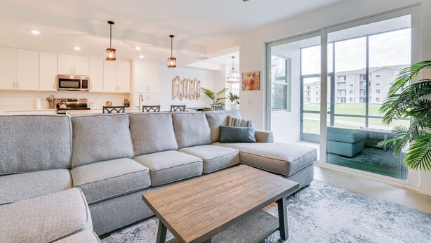 A modern living room with a sectional sofa, a wooden coffee table, and a large window offering a view of a residential area. - Ibis Landing Golf Club On-Site: Condo w/ Porch! (Lehigh Acres)