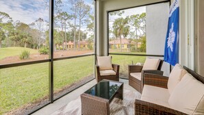 A room with large windows, wicker furniture, and a view of a grassy area and houses. - Ibis Landing Golf Club On-Site: Condo w/ Porch! (Lehigh Acres)
