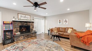 A living room with a stone fireplace, a ceiling fan, a couch, a coffee table, and arcade games. - County Club Townhome *Packman Game, Xbox, Golf course Views, Near Forest Edge (Flagstaff)