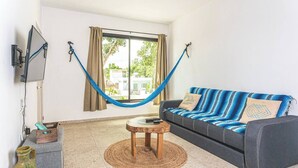 Uma sala de estar com uma rede, um sofá, uma televisão e uma mesinha.