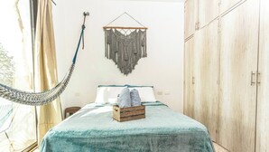 Quarto com cama, rede, tapeçaria de macramé e armários de madeira.