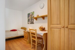 Une chambre à coucher avec un lit, un bureau en bois avec une chaise, une étagère fixée au mur et une porte.