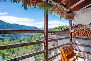 A balcony with a view of a mountainous landscape, a hanging basket with dried corn, and a metal railing.