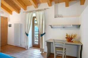 A room with a wooden ceiling, a desk with a chair, a radiator, and a window with curtains.