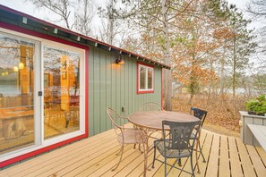 Un patio in legno con un tavolo e sedie in metallo, una porta in vetro e una finestra con cornice rossa.