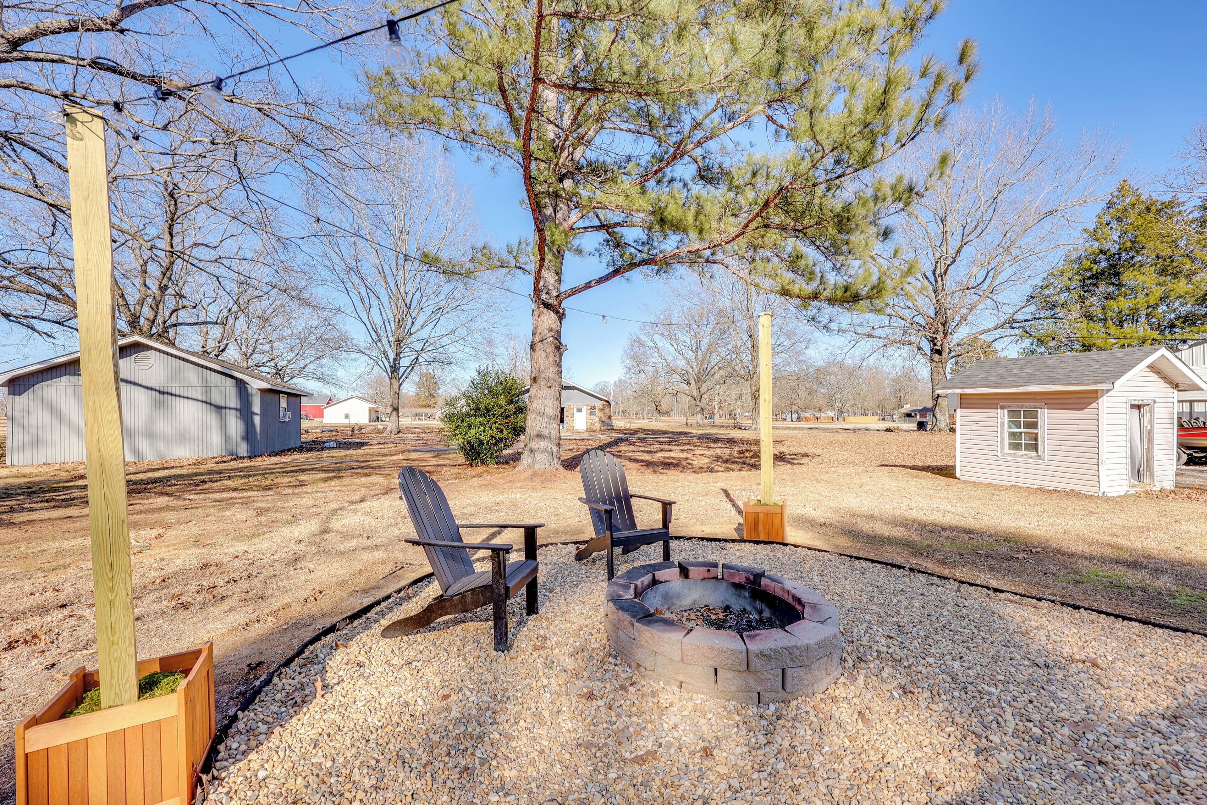 A backyard with a fire pit, two Adirondack chairs, and a wooden post.
