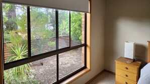 Une pièce avec une grande fenêtre, une commode en bois et une petite table de chevet.