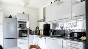 Une cuisine moderne avec des meubles blancs, un réfrigérateur en acier inoxydable, un four, un four à micro-ondes et un évier au-dessus duquel sont suspendus des ustensiles.