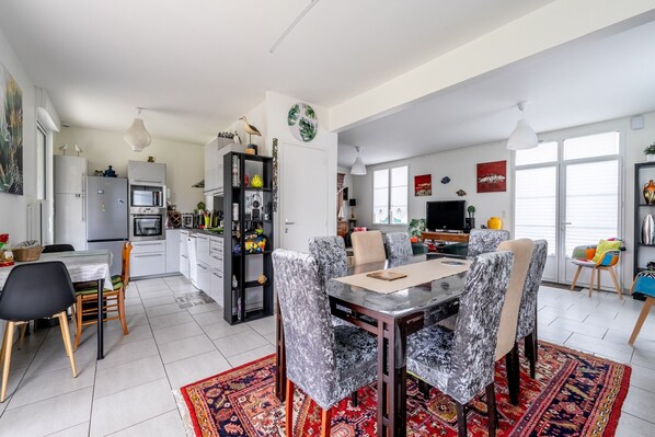 A modern kitchen with white cabinets, a dining area with a marble table and patterned chairs, and a living room with a TV and decorative items.