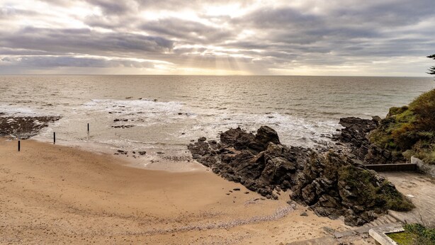Une plage avec des affleurements rocheux, une étendue de sable et un ciel nuageux.