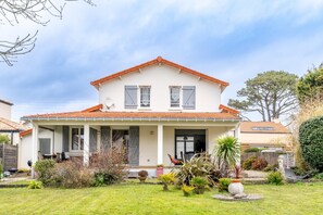 A two-story house with a red-tiled roof, a covered porch, and a well-maintained garden.