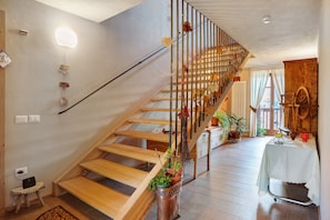 A wooden staircase with a metal railing, a small table with a laptop, and potted plants.
