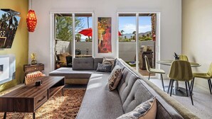 En moderne stue med sofa, sofabord og spiseplads. Store vinduer med udsigt til palmer og bjerge.