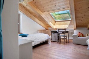A room with a sloped ceiling, a skylight, a bed, a desk, and a chair.