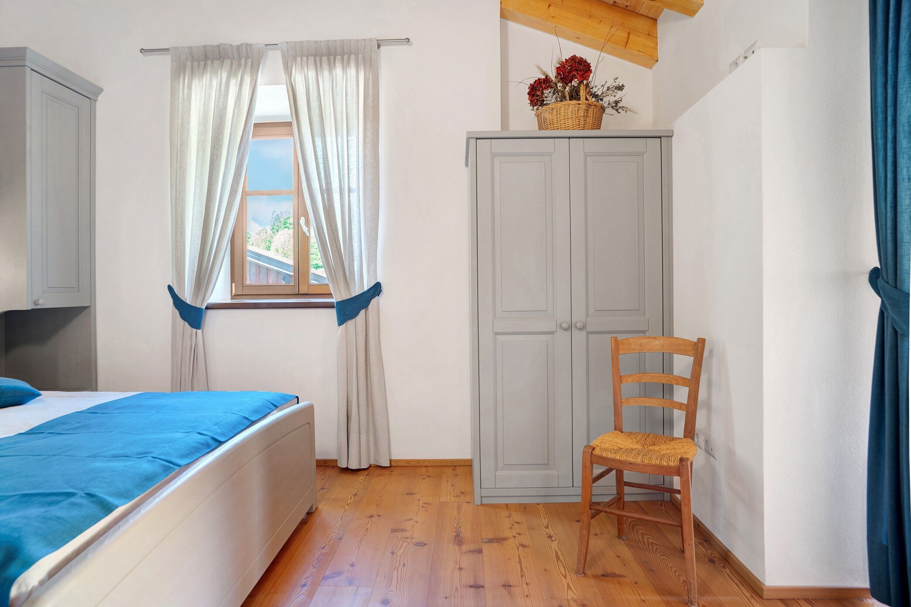 Ein Schlafzimmer mit einem Bett, einem Holzstuhl, einem Kleiderschrank und einem Fenster mit Vorhängen.