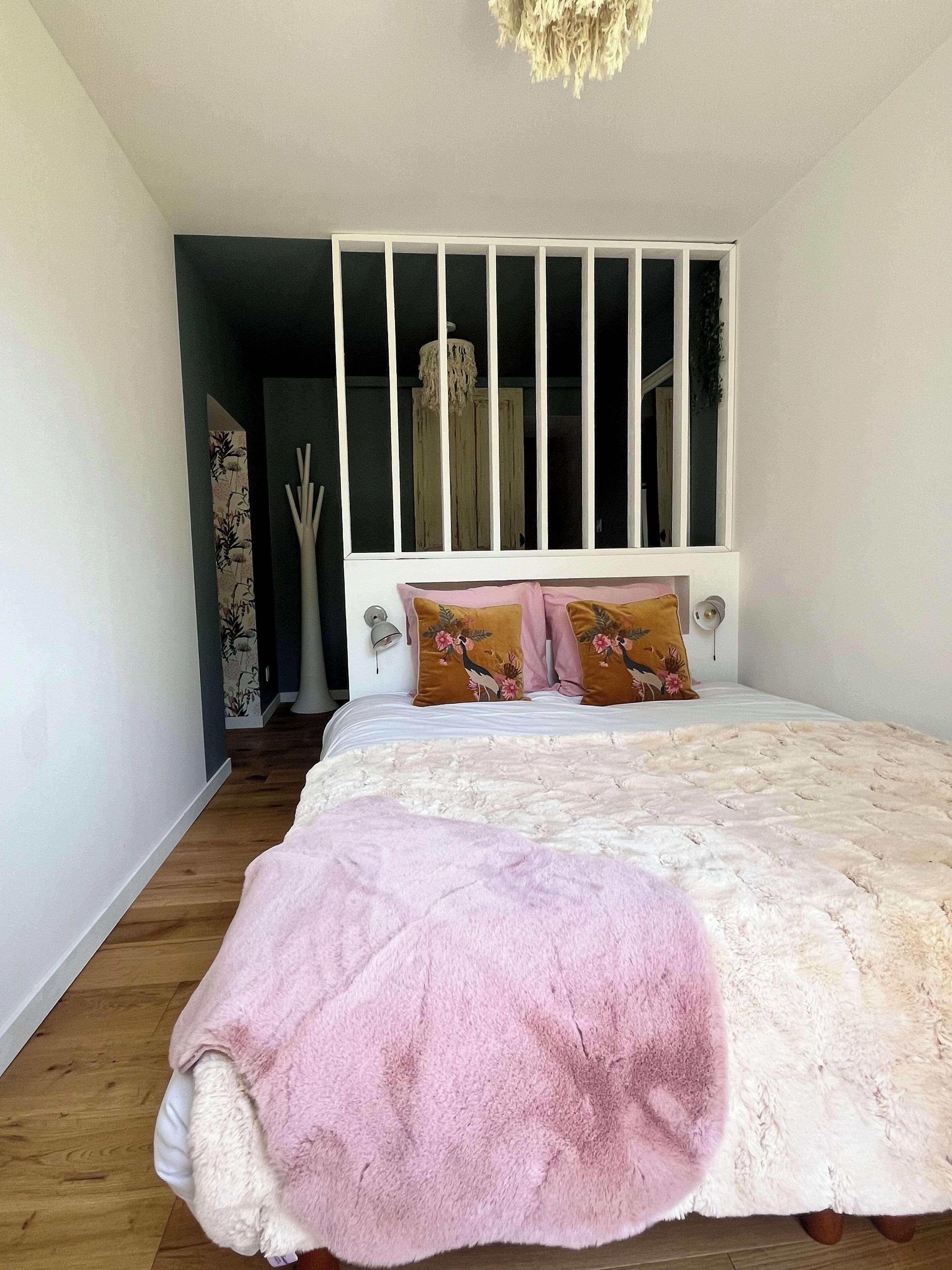 A bedroom with a white headboard, a pink blanket, and two floral pillows.