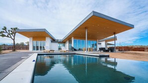 A modern house with a swimming pool, large windows, and a patio area. - Alto Yucca- Joshua Tree Modern Glass house with private pool (Yucca Valley)