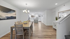 A modern kitchen with white cabinets, a wooden dining table, and a chandelier. - Modern Waters- Bright and Central- Walk to Downtown (Lake Geneva)