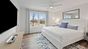 A bedroom with a bed, a ceiling fan, a window with curtains, a bedside table with a tray, and a mirror on the wall. - Modern Waters- Bright and Central- Walk to Downtown (Lake Geneva)