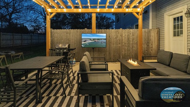 An outdoor patio with wooden furniture, a TV mounted on a wooden wall, and a fire feature.