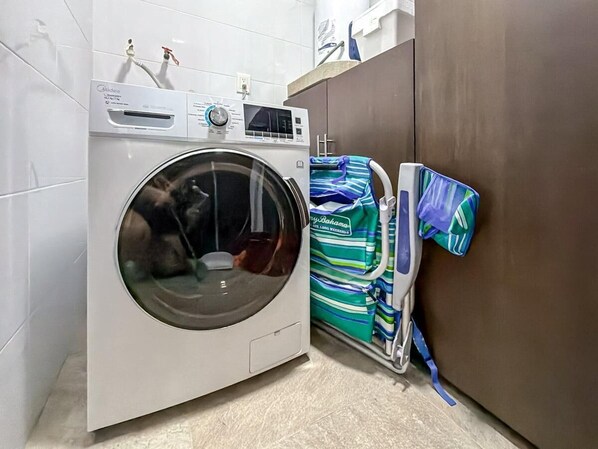 A compact, modern laundry room with a front-loading washing machine, a drying rack, and a cabinet.