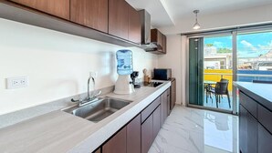 A modern kitchen with a large window, a water dispenser, and a view of a yellow building. - 2BR Condo w/Rooftop Pool (Isla Mujeres)