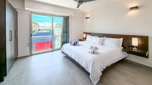A hotel room with a bed, ceiling fan, bedside lamp, and a view through a sliding glass door. - 2BR Condo w/Rooftop Pool (Isla Mujeres)