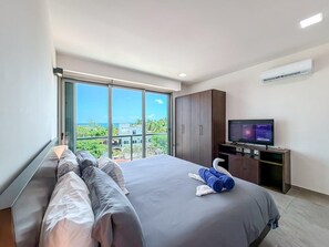 Quarto de hotel moderno com uma cama grande, televisão, guarda-roupa e varanda com vista para a cidade.