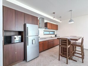 Una cocina moderna con armarios de madera oscura, un refrigerador de acero inoxidable, un microondas y un comedor con una mesa y sillas de madera.