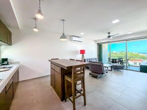 A modern kitchen with a dining area, a red lamp, and a view through large windows. - 1BR PH Downtown w/Rooftop Pool (Isla Mujeres)