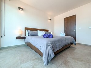 A modern bedroom with a large bed, a nightstand, and a wooden door.