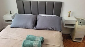 A neatly made bed with two pillows, a folded towel, and a bedside table with a small Eiffel Tower figurine and a vase with flowers. - SUH Copacabana 40 Smart Beach (Rio de Janeiro)