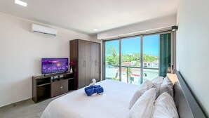 A hotel room with a large bed, a TV on a stand, a wardrobe, and a balcony with a view. - 1BR w/Rooftop Pool Downtown (Isla Mujeres)