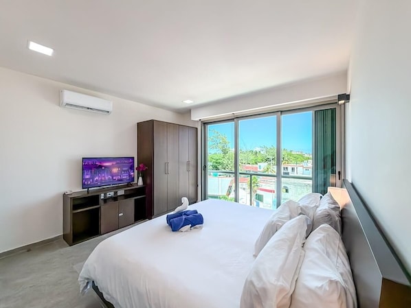 A hotel room with a large bed, a TV on a stand, a wardrobe, and a balcony with a view.
